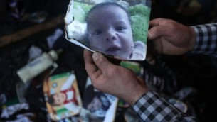 رجل يعرض صورة الرضيع الفلسطيني على سعد دوابشة البالغ من العمر 18 شهرا، والذي قُتل بعد إحراق منزل عائلته على يد متطرفين يهود في قرية دوما في الضفة الغربية، 31 يوليو، 2015. (AFP/Jaafar Ashtiyeh) 
