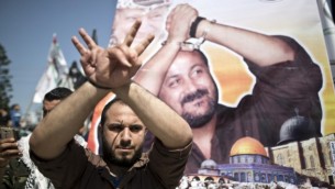 رجل فلسطيني يقف أمام ملصق يحمل صورة قيادي فتح والأسير في السجون الإسرائيلية مروان البرغوثي، خلال مسيرة لإحياء ’يوم الأسير الفلسطيني’ في مدينة غزة، 17 أبريل، 2016. (AFP/Mahmud Hams) 