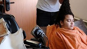 يمشط حمدي آمن شعر ابنته ماريا، التي أصيبت بالشلل، في منزلهم في حي بيت صفافا بالقدس في 23 أغسطس / آب 2017. (Judah Ari Gross/Times of Israel)