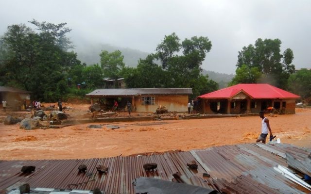 SIERRA LEONE-WEATHER-FLOOD A resident walks through floodwaters past a damaged building in an area of Freetown on August 14, 2017, after landslides struck the capital of the west African state of Sierra Leone. At least 312 people were killed and more than 2,000 left homeless when heavy flooding hit Sierra Leone's capital of Freetown, leaving morgues overflowing and residents desperately searching for loved ones. An AFP journalist at the scene saw bodies being carried away and houses submerged in two areas of the city, where roads turned into churning rivers of mud and corpses were washed up on the streets. / AFP PHOTO / SAIDU BAH