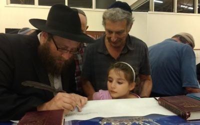Rabbi Gutnick writing in the Torah with Tony and Maggie Hakin looking on.