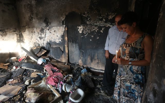 Israeli peace activists hold a candle in the Dawabsheh family's burnt-out home.
Photo: AFP Photo/Jaafar Ashtiyeh