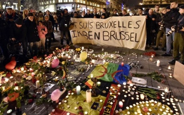 People holding a banner reading "I am Brussels" behind flowers and candles to mourn for the victims at Place de la Bourse in the centre of Brussels.