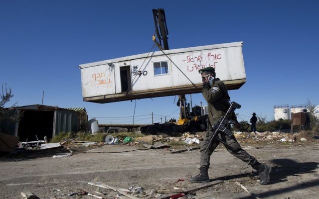 An Israeli border policeman walks near workers lifting a housing unit with a crane during the demolition of Amona on Tuesday. Photo: EPA/Abir Sultan
