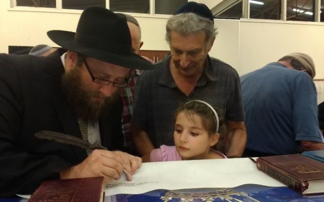 Rabbi Gutnick writing in the Torah with Tony and Maggie Hakin looking on.