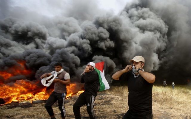 Palestinian protesters chant slogans next to a wall of smoke from burning tires designed to obstruct the view of the IDF who are trying to defend the border. Photo: AP Photo/Adel Hana