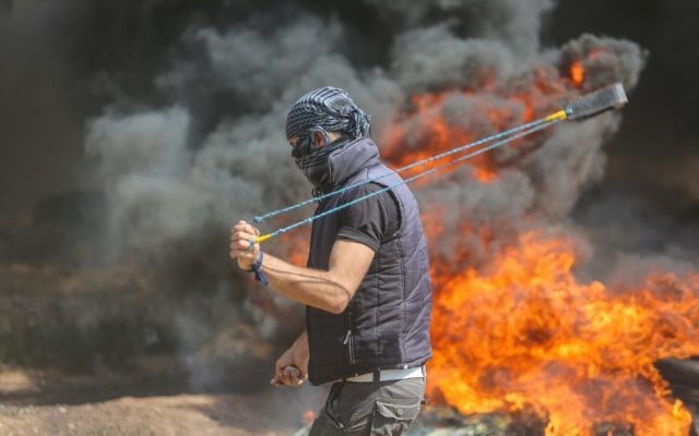 A Palestinian protester uses a sling to hurl stones towards Israeli forces during clashes along the Gaza border. Photo: AAP Image/CrowdSpark/Mhmed Ali