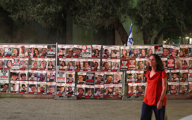 Illustrative: A woman walks past portraits of Israelis taken hostage by Palestinian terrorists in the October 7 attack, during a demonstration calling for their release in Tel Aviv on November 13, 2023. (The Times of Israel: Ahmad Gharabli/AFP)