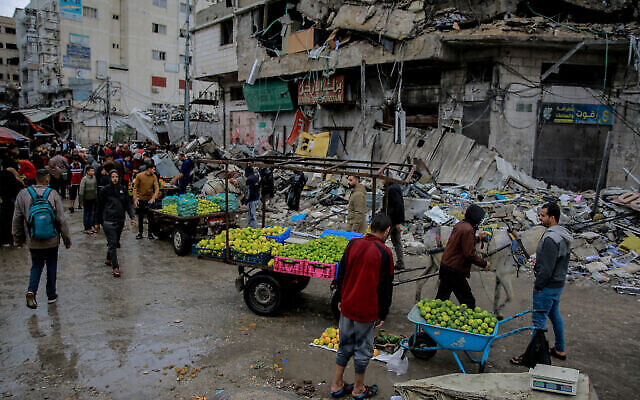 Palestinians sell vegetables in front of a destroyed building in Gaza City on November 27, 2023. (The Times of Israel: Omar El-Qattaa / AFP)