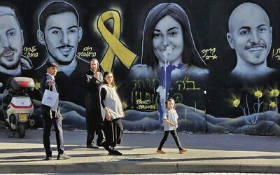Passersby in front of a mural depicting Israeli hostages in Jerusalem. Photo: Alan Meerkin