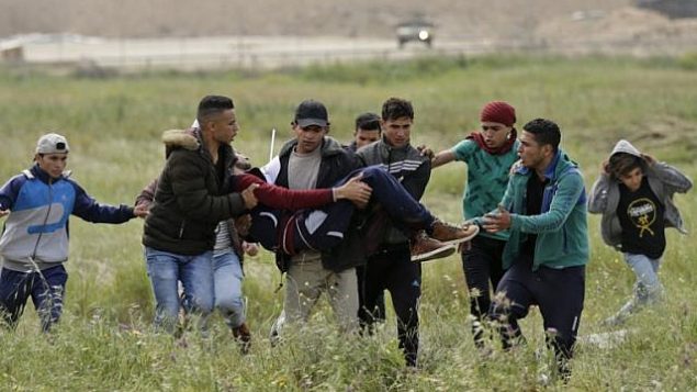متظاهرون يحملون شابا فلسطينيا أصيب خلال المواجهات، في أعقاب مظاهرة أجريت بالقرب من الحدود مع إسرائيل شرق مدينة غزة لإحياء ذكرى ’يوم الأرض’، 30 مارس، 2018. (AFP/ MAHMUD HAMS)