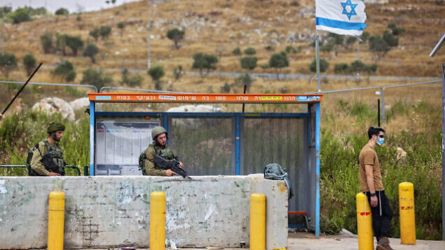 نود إسرائيليون يحرسون محطة حافلات عند مفرق تبواح بالقرب من مدينة نابلس في الضفة الغربية، 30 يونيو، 2020. (AP / Oded Balilty)
