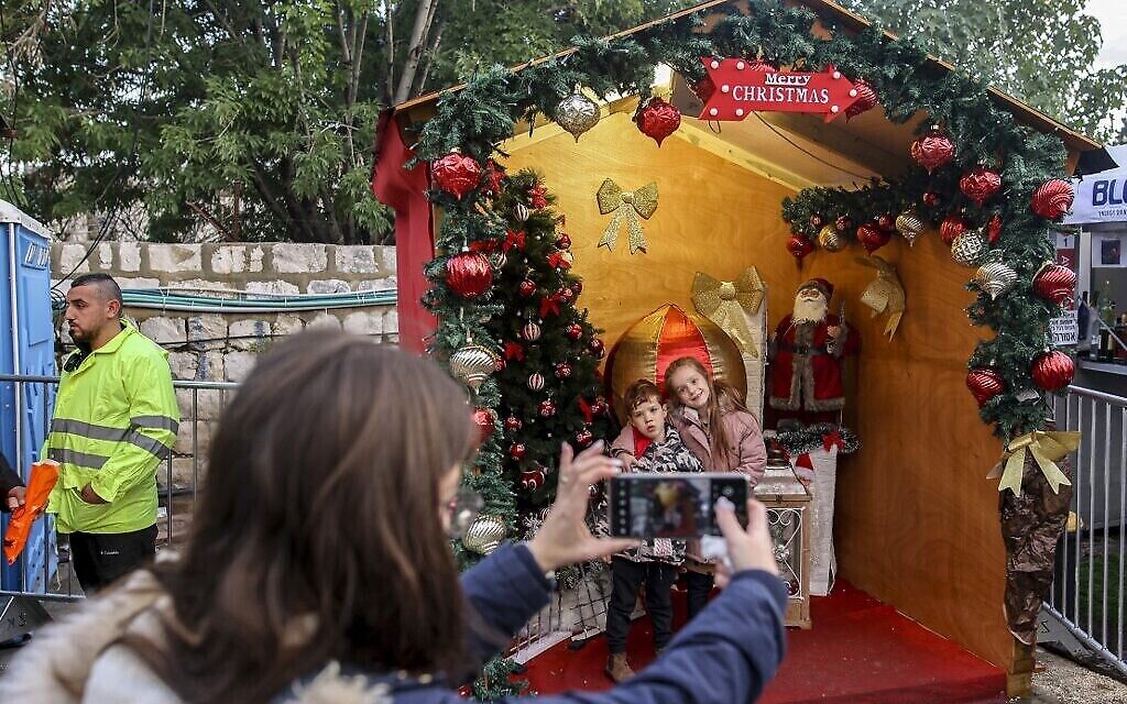 أطفال يقفان لالتقاط صور لهما مع المذود وشجرة عيد الميلاد والقديس نيكولاس (سانتا كلوز) في وسط مدينة الناصرة شمال إسرائيل، 18 ديسمبر، 2021. (AHMAD GHARABLI / AFP)
