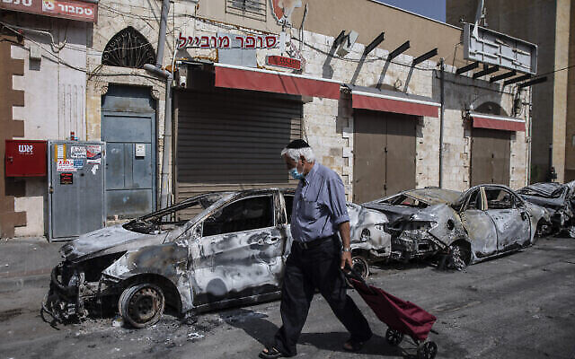 رجل يمر بجانب سيارات أضرمت فيها النيران بعد ليلة من أعمال العنف بين متظاهرين من عرب إسرائيل والشرطة الإسرائيلية في بلدة اللد المختلطة بين العرب واليهود، وسط إسرائيل، يوم الثلاثاء، 11 مايو، 2021 (AP Photo / Heidi Levine)
