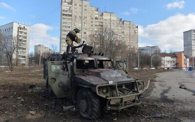 An Ukrainian Territorial Defence fighter examines a destroyed Russian infantry mobility vehicle GAZ Tigr after the fight in Kharkiv on February 27, 2022. - Ukrainian forces secured full control of Kharkiv on February 27, 2022 following street fighting with Russian troops in the country's second biggest city, the local governor said. (Photo by Sergey BOBOK / AFP)