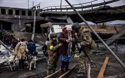 جنود أوكرانيون يساعدون امرأة مسنة في عبور جسر مدمر أثناء إجلائها من مدينة إيربين، شمال غرب كييف، 7 مارس، 2022.(Dimitar DILKOFF / AFP)