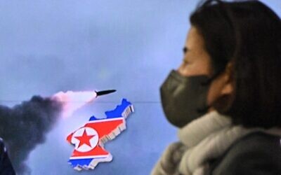 امرأة تمر أمام تقرير تلفزيوني يظهر بثًا إخباريًا يتضمن لقطات  لاختبار صاروخ كوري شمالي، في سيول، 24 مارس 2022 (Anthony WALLACE / AFP)