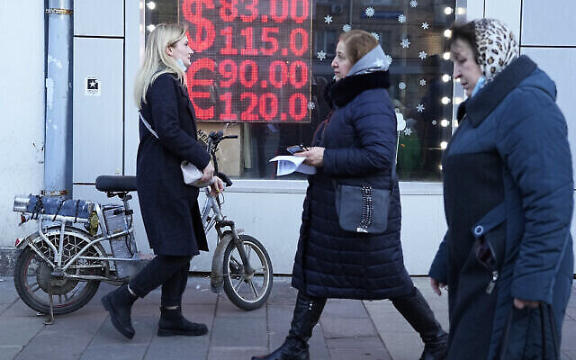 أشخاص يمرون عبر شاشة مكتب صرف عملات تعرض أسعار صرف الدولار الأمريكي واليورو مقابل الروبل الروسي في وسط مدينة موسكو، روسيا، يوم الاثنين 28 فبراير 2022 (AP / Pavel Golovkin)
