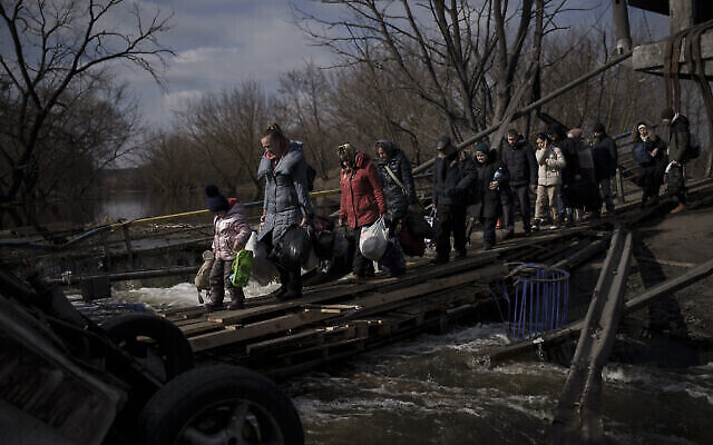 أوكرانيون يعبرون طريقا مرتجلا تحت جسر مدمر أثناء فرارهم من إيربين، في ضواحي كييف، أوكرانيا، 9 مارس، 2022. (AP Photo/Felipe Dana)