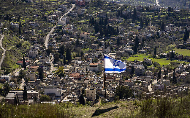 في الصورة تظهر قرية برقة الفلسطينية، وعلم إسرائيلي تم وضعه في بؤرة حومش الاستيطانية بالضفة الغربية، 17 يناير، 2022. (AP/Ariel Schalit)