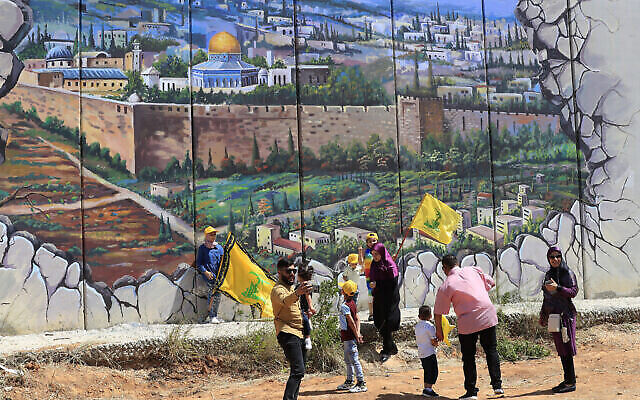 أنصار حزب الله يلوحون بالأعلام أمام ملصق يُظهر قبة الصخرة والمسجد الأقصى في الحرم القدسي، رسم على جدار حدودي بنته إسرائيلي، بمناسبة الذكرى الثانية والعشرين لانسحاب إسرائيل من جنوب لبنان في 25 مايو 2000، في قرية كفر كلا، جنوب لبنان، الأربعاء 25 أيار 2022 (AP Photo / Mohammed Zaatari)