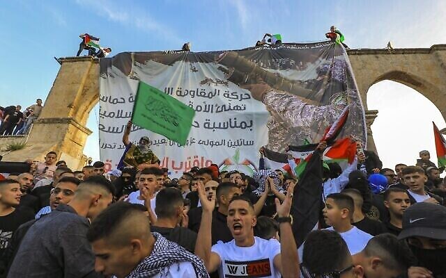 فلسطينيون يرددون شعارات مؤيدة لحماس بعد صلاة عيد الفطر أمام لافتة للحركة في المسجد الأقصى بالقدس، 2 مايو، 2022. (Jamal Awad/Flash90)
