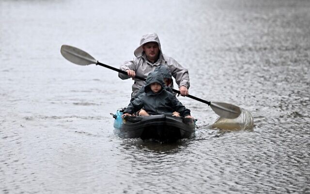 أشخاص يستخدمون قوارب الكاياك على طول شارع غمرته المياه من نهر هاوكيسبيري الفائض بسبب الأمطار الغزيرة في ضاحية وندسور في سيدني، 4 يوليو، 2022. ( SAEED KHAN / AFP)