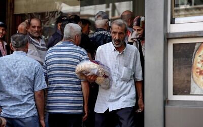 رجل يخرج من مخبز يحمل كيس خبز مدعوم من الحكومة، بينما يواصل الآخرون الانتظار في طابور، في العاصمة اللبنانية بيروت، 29 يوليو 2022 (JOSEPH EID / AFP)