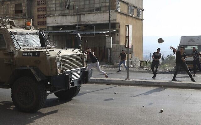 شبان فلسطينيون يرشقون مركبات عسكرية بالحجارة خلال عملية عسكرية للجيش الاسرائيلي لاعتقال مطلوبين من مخيم بلاطة بالقرب من مدينة نابلس بالضفة الغربية، 17 اغسطس، 2022. (JAAFAR ASHTIYEH / AFP)