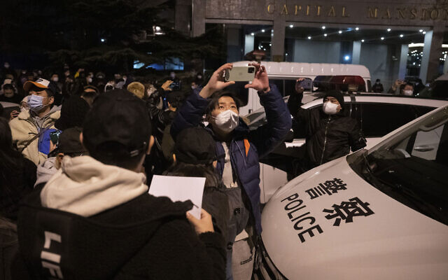 متظاهرون ضد قواعد الصين الصارمة لمكافحة فيروس كورونا يمرون بالقرب من سيارة للشرطة في بكين، 27 نوفمبر 2022 (AP Photo / Ng Han Guan)