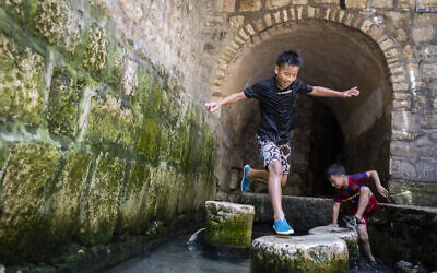 أطفال من تايوان يلعبون في مياه بركة سلوان بعد المشي في نفق حزقيا خلال زيارتهم لمتنزه مدينة داود الوطني، 28 يوليو 2019 (Hadas Parush / Flash90)