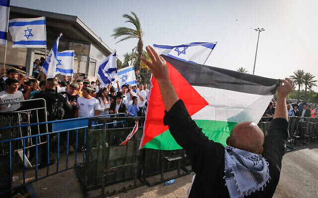 رجل يحمل العلم الفلسطيني يقف أمام متظاهرين يرفعون الأعلام الإسرائيلية بالقرب من البلدة القديمة في القدس خلال احتفالات "يوم أورشليم"، 29 مايو، 2022. (Jamal Awad / Flash90)