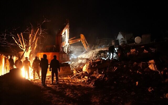 عمال الإنقاذ يستريحون بجانب حريق بينما يواصل آخرون الحفر في أنقاض مبنى في بلدة الجنديريس السورية التي تسيطر عليها المعارضة، بعد يومين من الزلزال المدمر الذي ضرب تركيا وسوريا، 8 فبراير 2023 (Rami al SAYED / AFP)