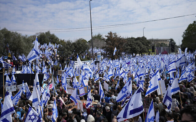 إسرائيليون يلوحون بالأعلام الوطنية خلال احتجاج على خطط حكومة رئيس الوزراء بنيامين نتنياهو الجديدة لإصلاح النظام القضائي، خارج الكنيست في القدس، 13 فبراير 2023 (AP / Ohad Zwigenberg)