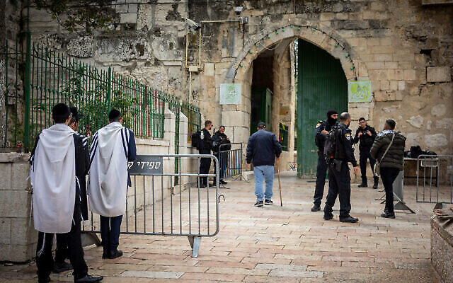 رجال يهود متشددون، على يسار الصورة، يؤدون الصلاة بينما يقف أفراد في الشرطة الإسرائيلية لحراسة مدخل المسجد الأقصى، في البلدة القديمة بالقدس، 19 أبريل، 2022. (Yonatan Sindel / Flash90)