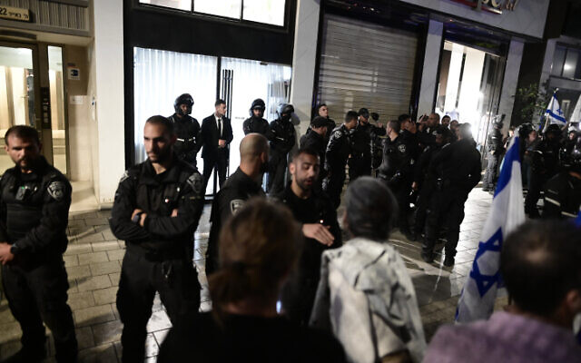 ضباط الشرطة يحرسون بينما الناس يتظاهرون ضد زوجة رئيس الوزراء سارة نتنياهو، خارج صالون لتصفيف الشعر في تل أبيب، 1 مارس 2023 (Avshalom Sassoni / Flash90)