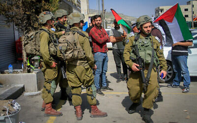 توضيحية: فلسطينيون يواجهون جنودا إسرائيليين وهم يلوحون بالأعلام الفلسطينية وسط بلدة حوارة بالضفة الغربية، 2 مارس، 2023. (Nasser Ishtayeh / Flash90)