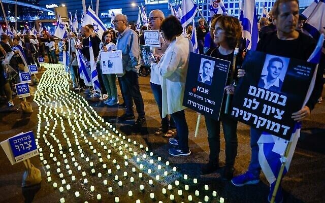 عائلات ثكلى وإسرائيليون آخرون يقفون بجانب شموع تذكارية خلال احتجاج على الإصلاح القضائي الذي تخطط له الحكومة الإسرائيلية، في تل أبيب، 22 أبريل، 2023. (Erik Marmor / Flash90)
