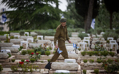 جندي إسرائيلي يضع الزهور والشموع على قبور الجنود القتلى في المقبرة  العسكرية بجبل هرتسل  في القدس، 23 أبريل، 2023،  عشية يوم ذكرى قتلى معارك إسرائيل وضحايا الأعمال العدائية. (Yonatan Sindel / Flash90)