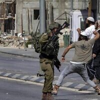 توضيحية: جنود اسرائيليون يقفون وقفة المتفرج بينما يرشق مستوطنون فلسطينيين بالحجارة خلال مواجهات في بلدة حوارة بالضفة الغربية، 13 أكتوبر، 2022. (Oren Ziv / AFP)