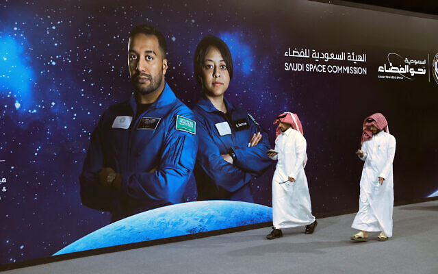أشخاص يمشون أمام ملصق عليه صورة رائدي الفضاء في هيئة الفضاء السعودية علي القرني (يسار) وريانة برناوي، من بعثة "أكسيوم 2"، في حفل مشاهدة نظمته الحكومة في الرياض، 21 مايو 2023 (Fayez Nureldine/AFP)