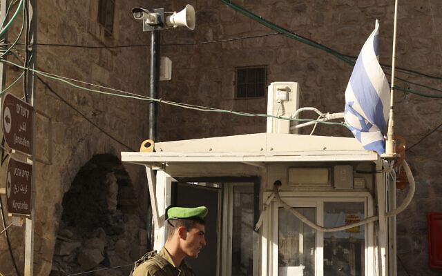 جندي إسرائيلي يقف تحت كاميرا مراقبة عند نقطة تفتيش في مدينة الخليل الفلسطينية، 9 نوفمبر 2021 (HAZEM BADER / AFP)
