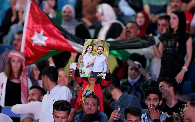 رجل يرفع ملصقًا قبل يحمل صورة ولي العهد الأردني الأمير حسين وخطيبته رجوة آل سيف ، خلال حفل موسيقي مجاني للاحتفال بالزفاف المرتقب في استاد عمان الدولي، 29 مايو، 2023. (Khalil MAZRAAWI / AFP)