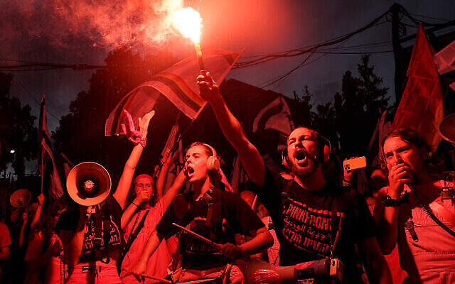 متظاهر من مجموعة 'Pink Front' يضيء شعلة بينما يدق آخرون في فرقة موسيقية على الطبول خلال احتجاج على خطة الإصلاح القضائي للحكومة الإسرائيلية في تل أبيب، 8 يوليو، 2023. (JACK GUEZ / AFP)