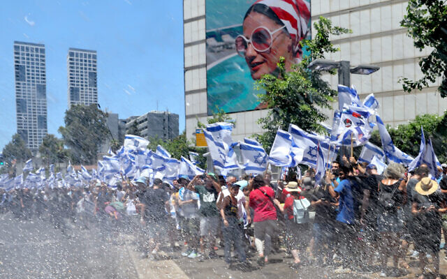 متظاهرون يلوحون بالأعلام الإسرائيلية بينما يتعرضون لخراطيم مياه الشرطة، خلال مظاهرة في تل أبيب، 11 يوليو 2023 (JACK GUEZ / AFP)