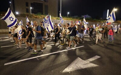 متظاهرون يحملون الأعلام الإسرائيلية على  طريق سريع بالقرب من تل أبيب خلال مظاهرة ضد خطة الحكومة الإسرائيلية للإصلاح القضائي، 18 يوليو، 2023. (JACK GUEZ / AFP)