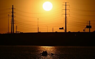 الشمس تغرب خلف خطوط الكهرباء بينما يتجول الناس على بحيرة تيمبي تاون خلال موجة حرارة قياسية في تيمبي، أريزونا، 18 يوليو 2023 (Patrick T. Fallon / AFP)