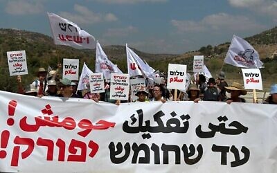 نشطاء يساريون يسيرون باتجاه حومش، 7 يوليو، 2023، حاملين لافتة كتب عليها بالعبرية والعربية "حتى يتم تفكيك حومش". (Courtesy Peace Now)
