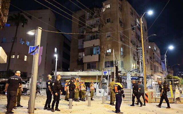 قوات أمن إسرائيلية وعمال إنقاذ يتجمعون أمام مبنى في تل أبيب أصيب بصاروخ أطلق من قطاع غزة، 7 أكتوبر، 2023. (JACK GUEZ / AFP)