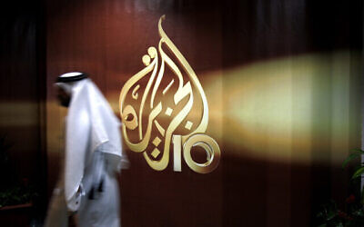 توضيحية: أحد موظفي قناة الجزيرة يمر أمام شعار القناة في مقرها الرئيسي في الدوحة، قطر، عام 2006. (AP/Kamran Jebreili, File)